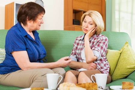 Two women sitting on green couch talking. One seems very sad.