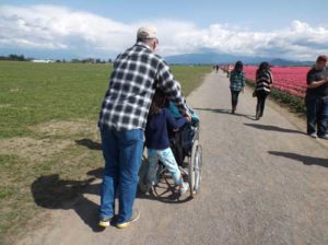 Man pushing Mom in wheelchair; little girl riding the back; seeing tulips in WA