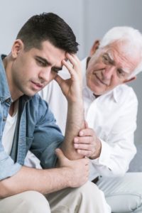 A gray-haiired man offers comfort. to a young man.