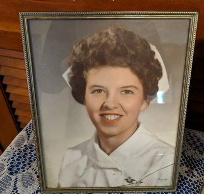 Framed picture of a young Karen Baker in a nurse's uniform sitting on a crocheted tablecloth.