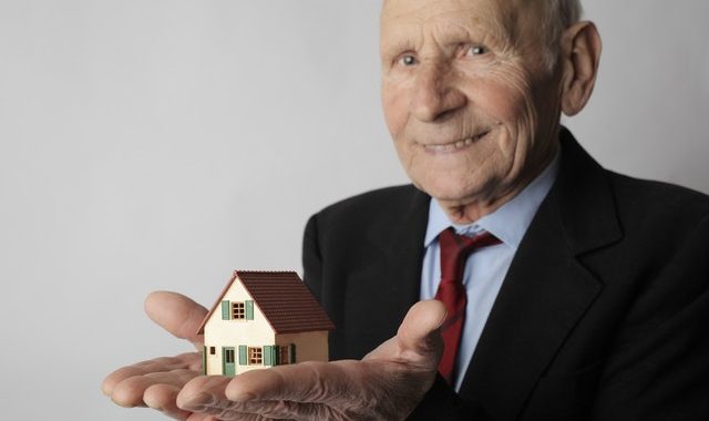 Older man holding model of house in hus hands.