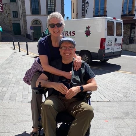 Danny van Leeuwen and his wife, both smiling. He is in his wheelchair. She is standing behind him with her arms around his shoulders.