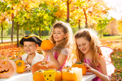 2 girls and a boy smiling and carving and decoating pumpkins on an autumn day.