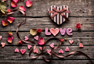 "Love" with flower petals and heart candy box on wooden board.