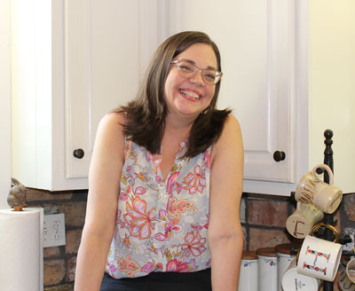 Casual picture of Sallie Belle Howell, smiling, standing in her kitchen.