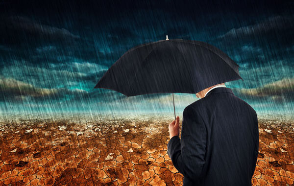 Man with umbrella standing in rainstorm. Blue sky with dark clouds. Golden ground.