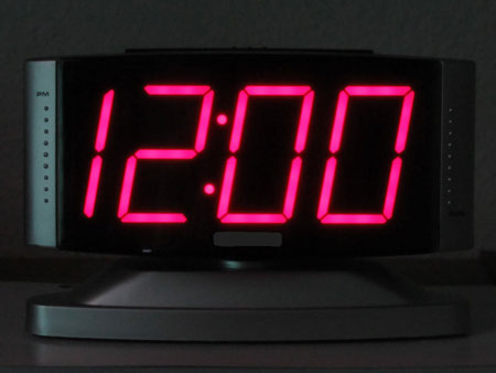 Black clock with pink numerals showing 12:00