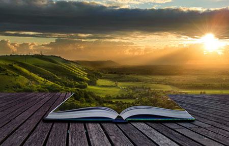 Open book on wooden porch with beautiful sunny scene coming out of it.